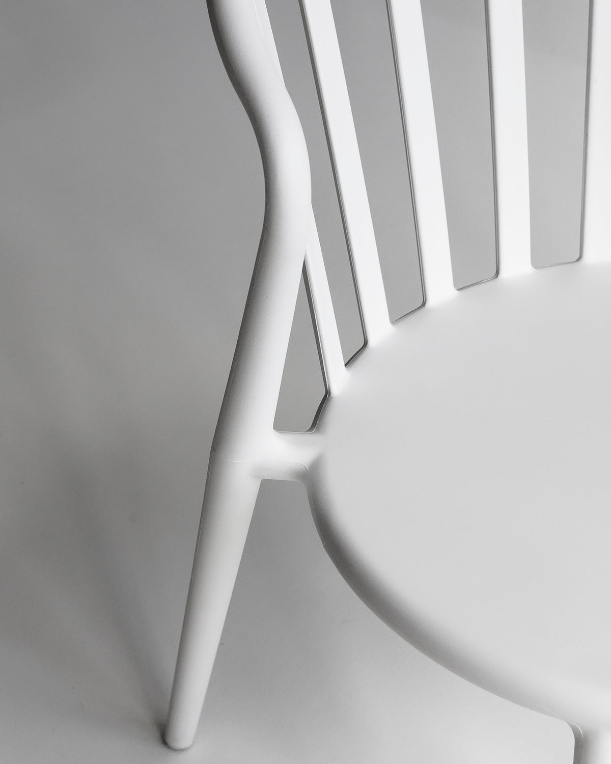 Close-up of white Cleo chair showing curved backrest and moulded polypropylene legs