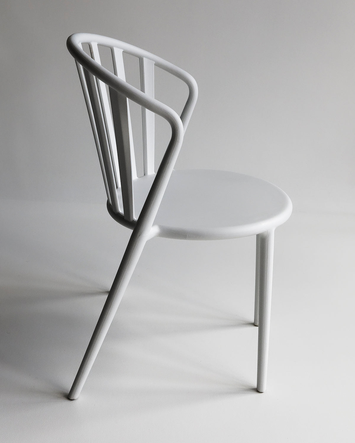 White Cleo chair shown from the side in a studio setting, highlighting its slim profile and curved seat