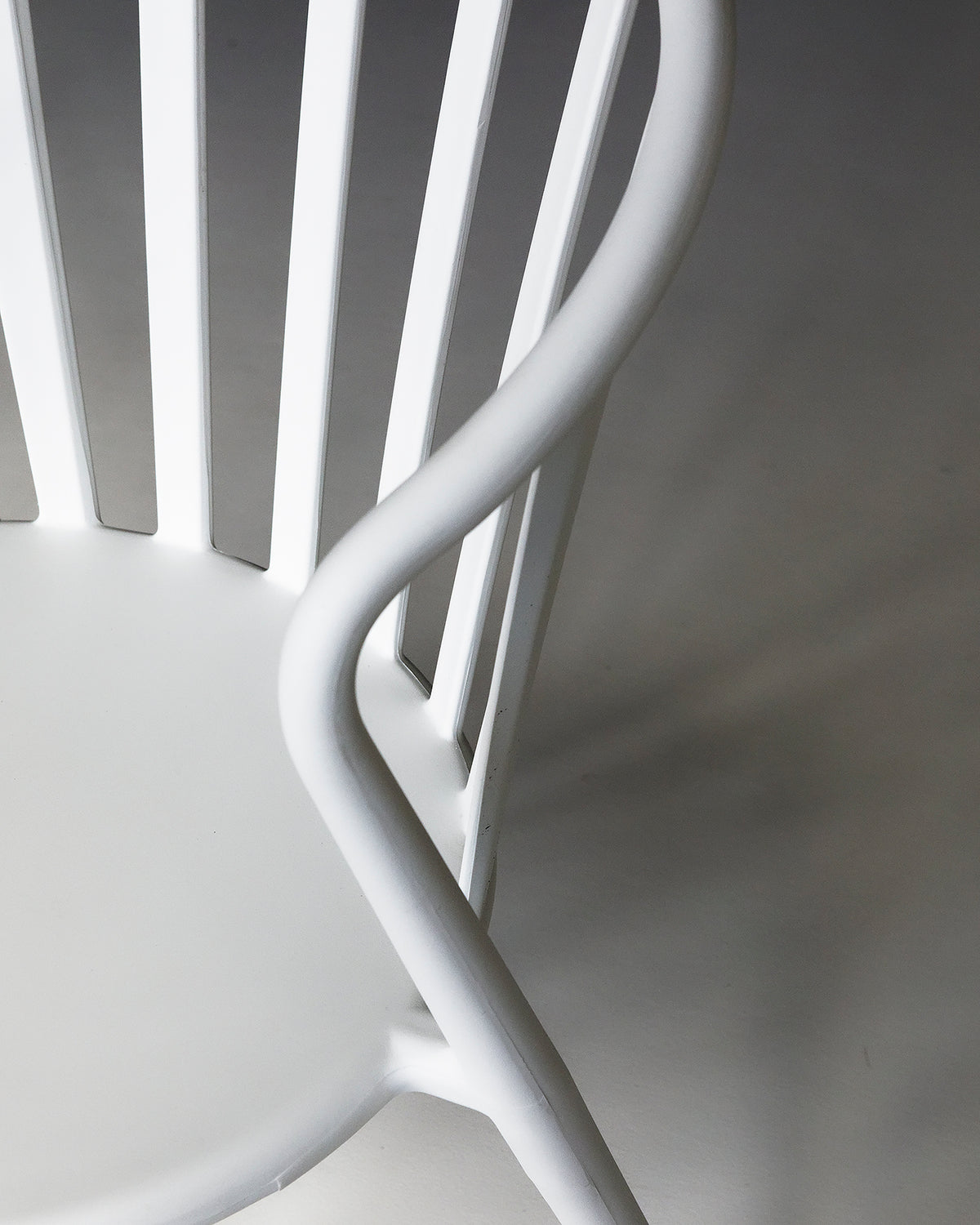 White Cleo chair shown from the side in a studio setting, highlighting its slim profile and curved seat