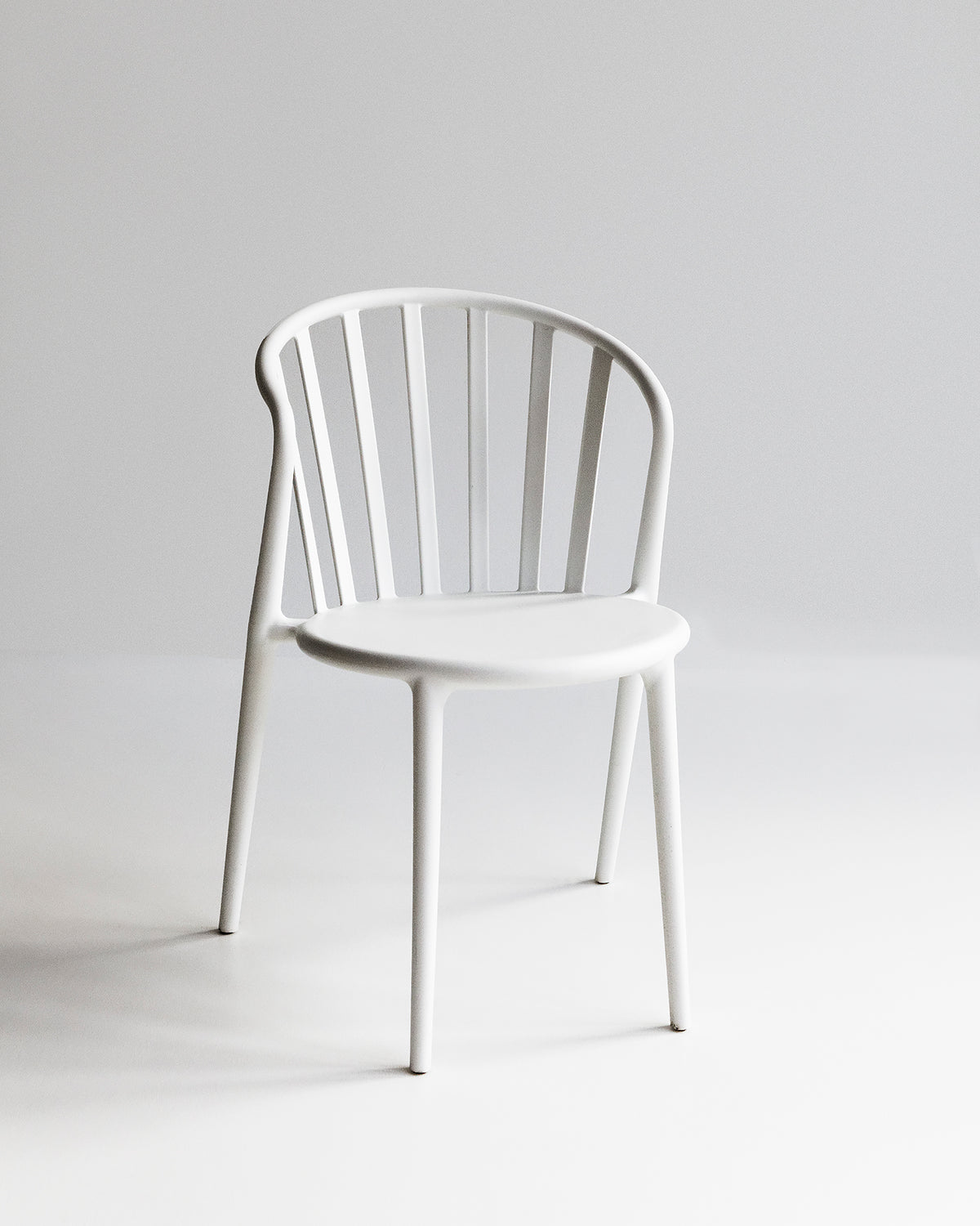 White Cleo dining chair photographed front-on, showing slim silhouette and curved backrest for indoor and outdoor use
