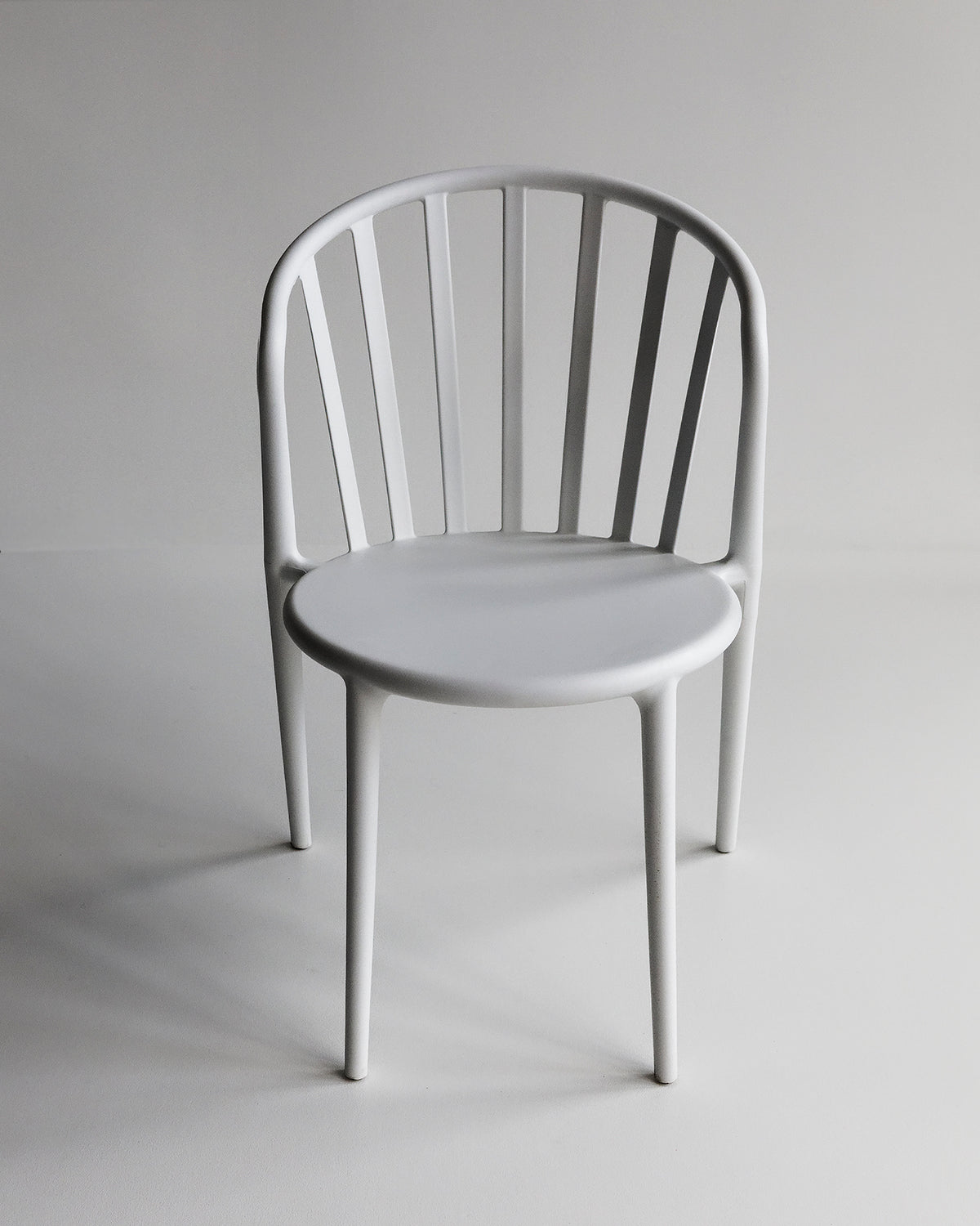 White Cleo dining chair shown front-on in a studio setting, featuring a gently curved seat and slim, modern profile