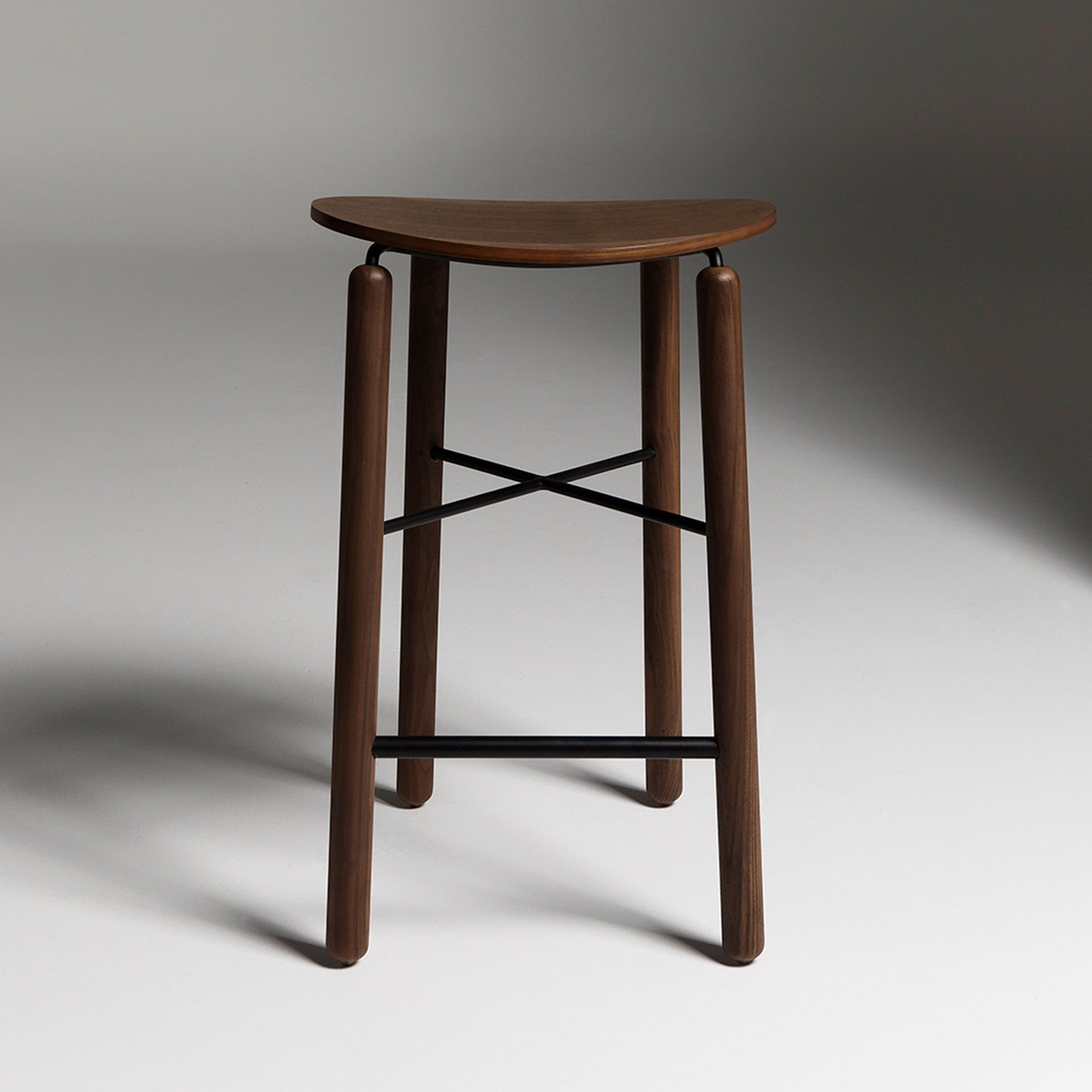 Walnut Greta stool photographed front-on, showing rich timber seat and slim metal base