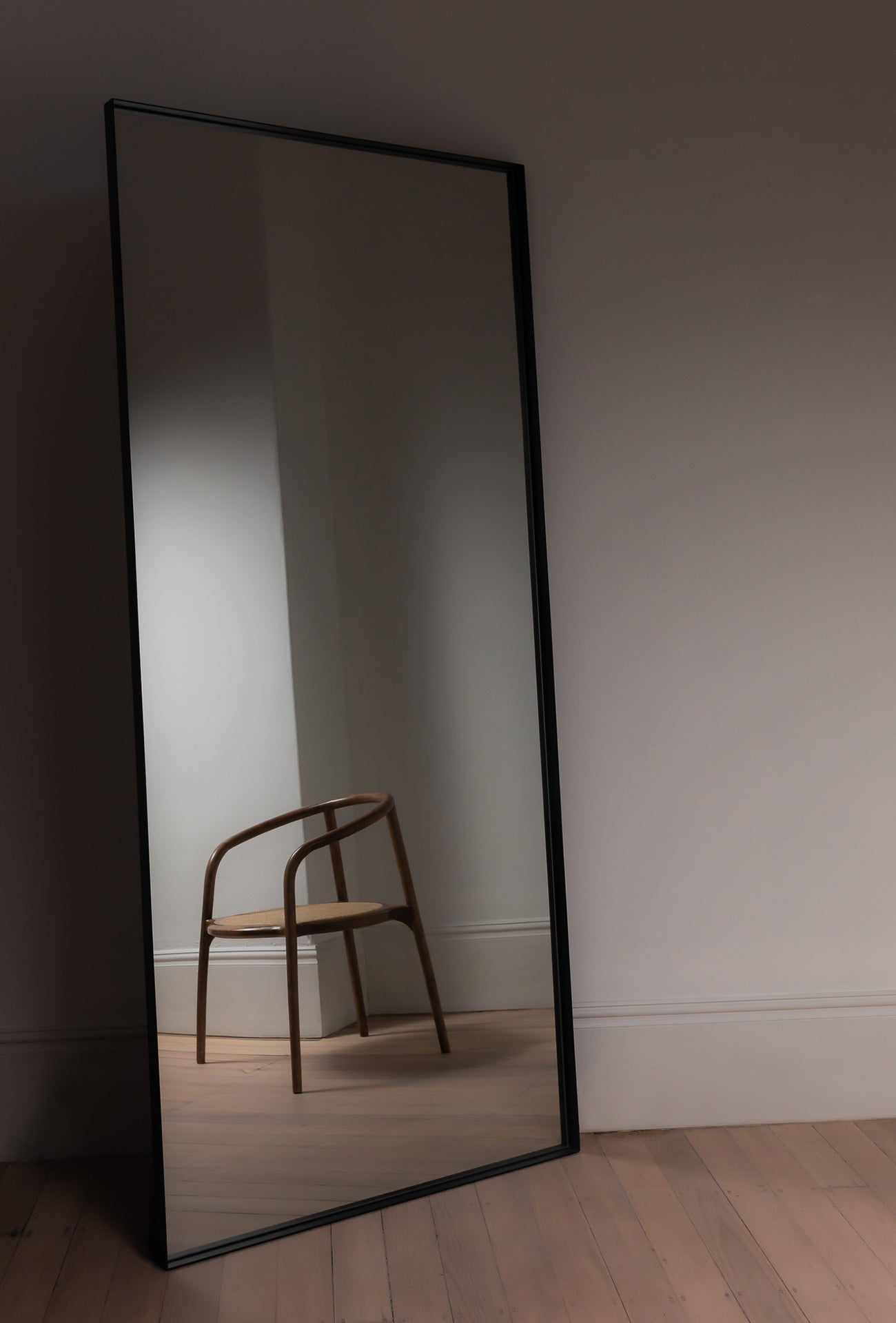 Luca Mirror in Black leaning against a wall in a styled hallway, reflecting natural light
