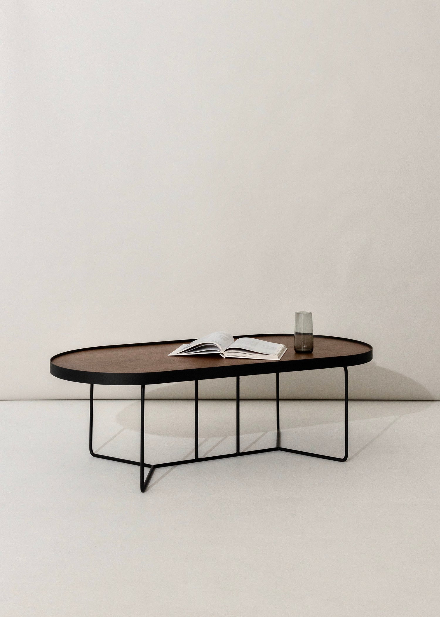 Studio shot of the Sia Oval Coffee Table in Walnut, front view showing deep-etched timber top and slim base