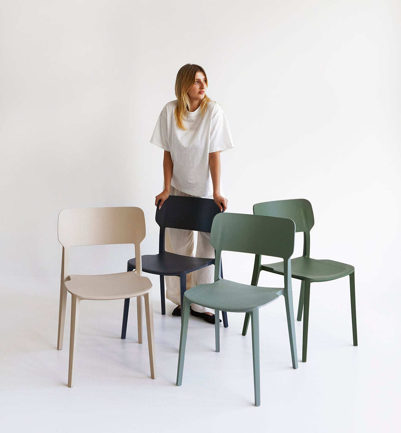 Woman standing next to a variety of chairs in different colors on a white background