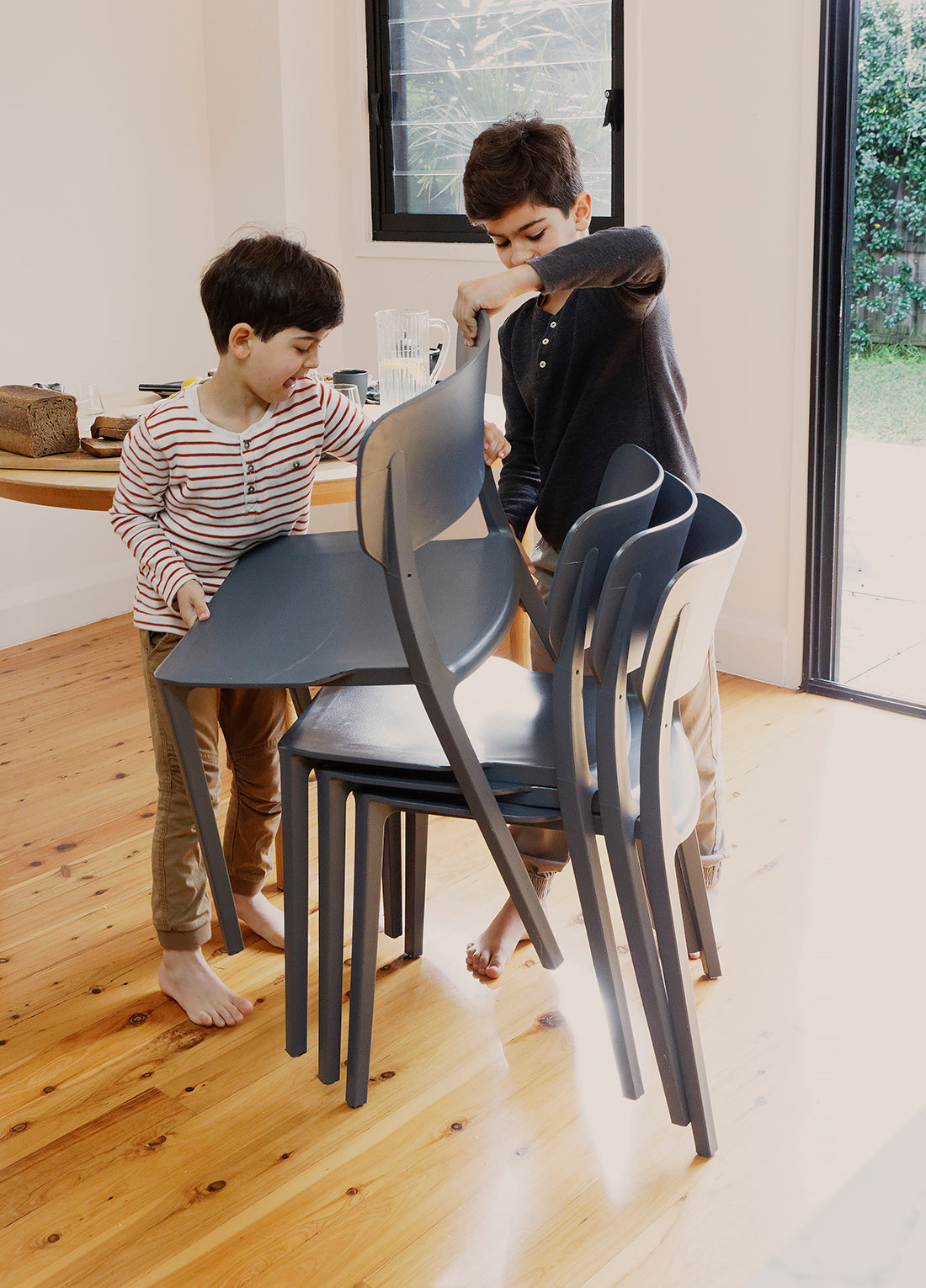  Kids helping to stack Charcoal Alex Chairs after a meal, showing their light weight, easy handling, and suitability for everyday family life.