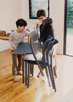  Kids helping to stack Charcoal Alex Chairs after a meal, showing their light weight, easy handling, and suitability for everyday family life.