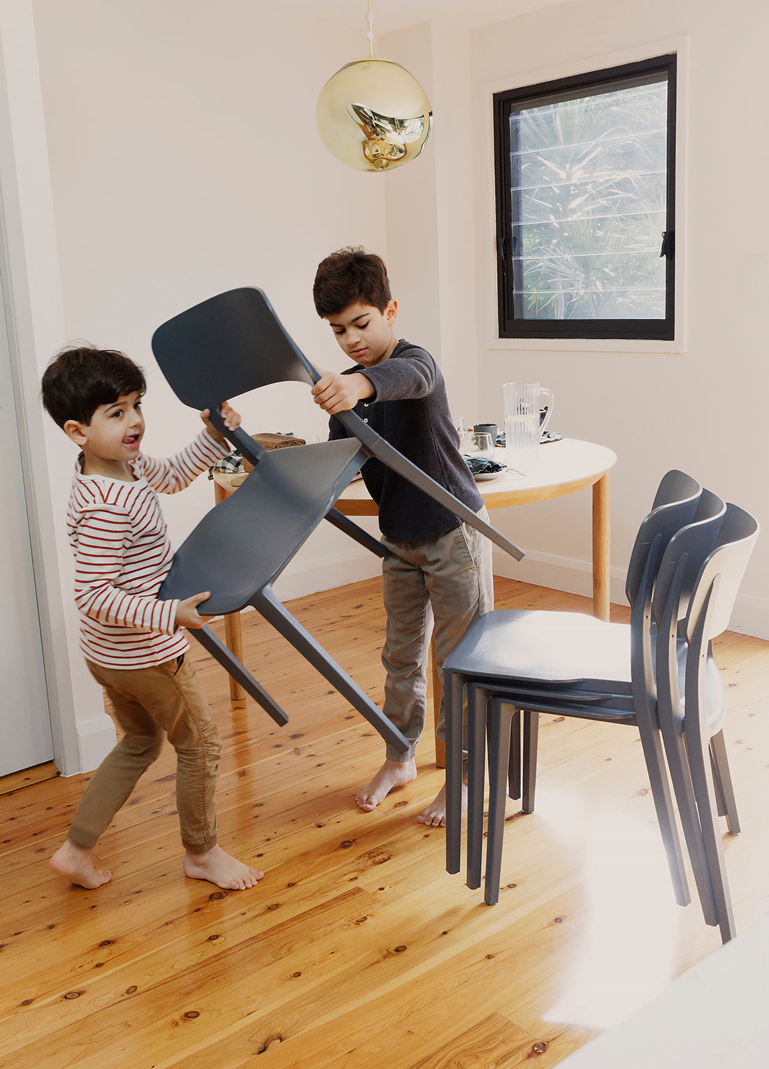 Children playfully stacking Charcoal Alex Chairs in a family home setting, highlighting the chairs’ lightweight, easy-to-move design and family-friendly functionality.