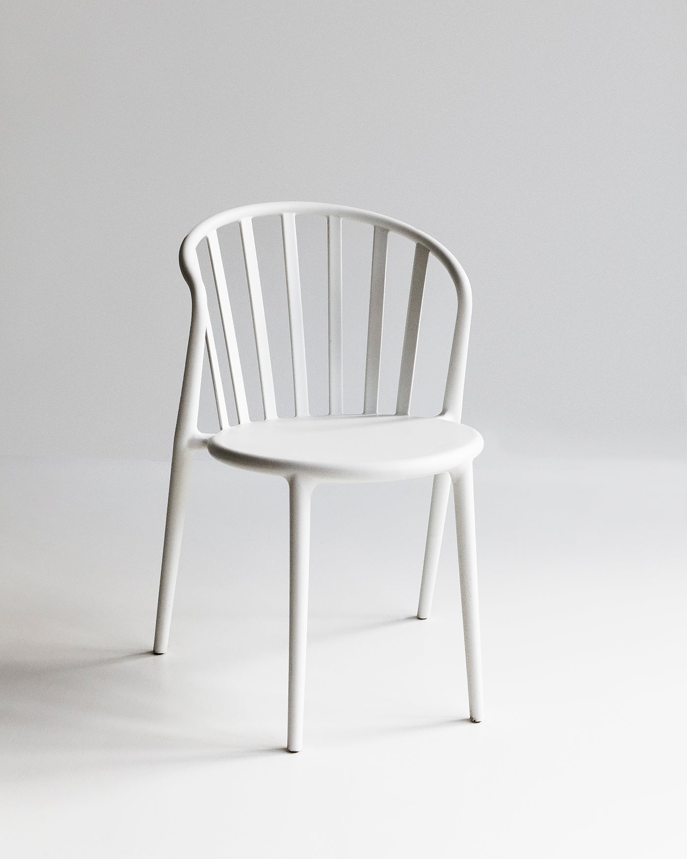 White Cleo dining chair photographed front-on, showing slim silhouette and curved backrest for indoor and outdoor use