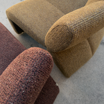 A close-up of textured woven upholstery in two tones: a tan/olive-brown armchair section in the background and a darker reddish-brown cushion in the foreground, photographed on a concrete floor.