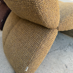Close-up of a textured boucle fabric armrest cushion in a warm tan-brown color, with a small white brand tag reading 'suedo' visible near the bottom edge.