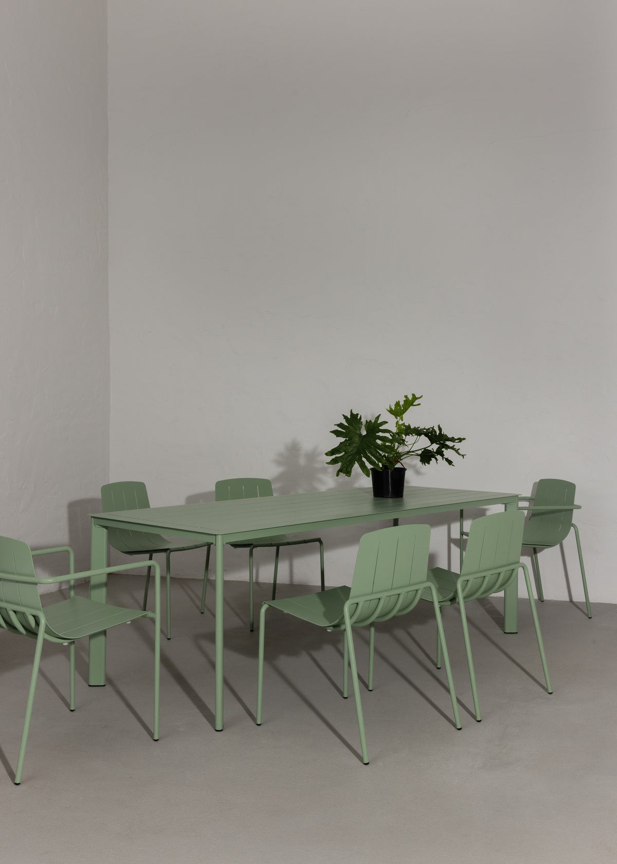 Green outdoor furniture set with table and chairs against a plain wall.