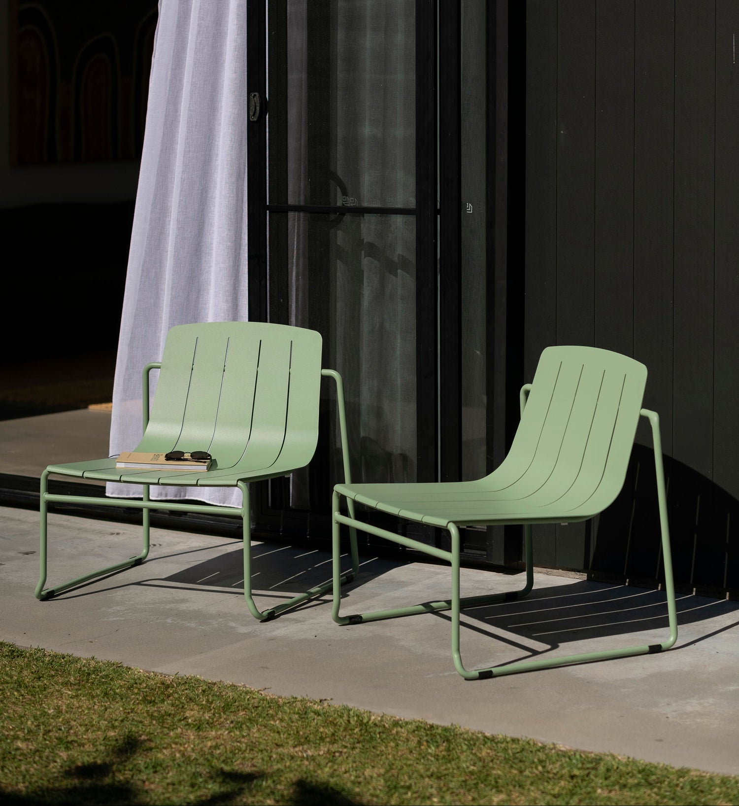 Two green chairs on a patio with a dark wall and white curtain in the background.