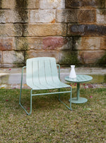 Light green outdoor chair and table set against a stone wall.