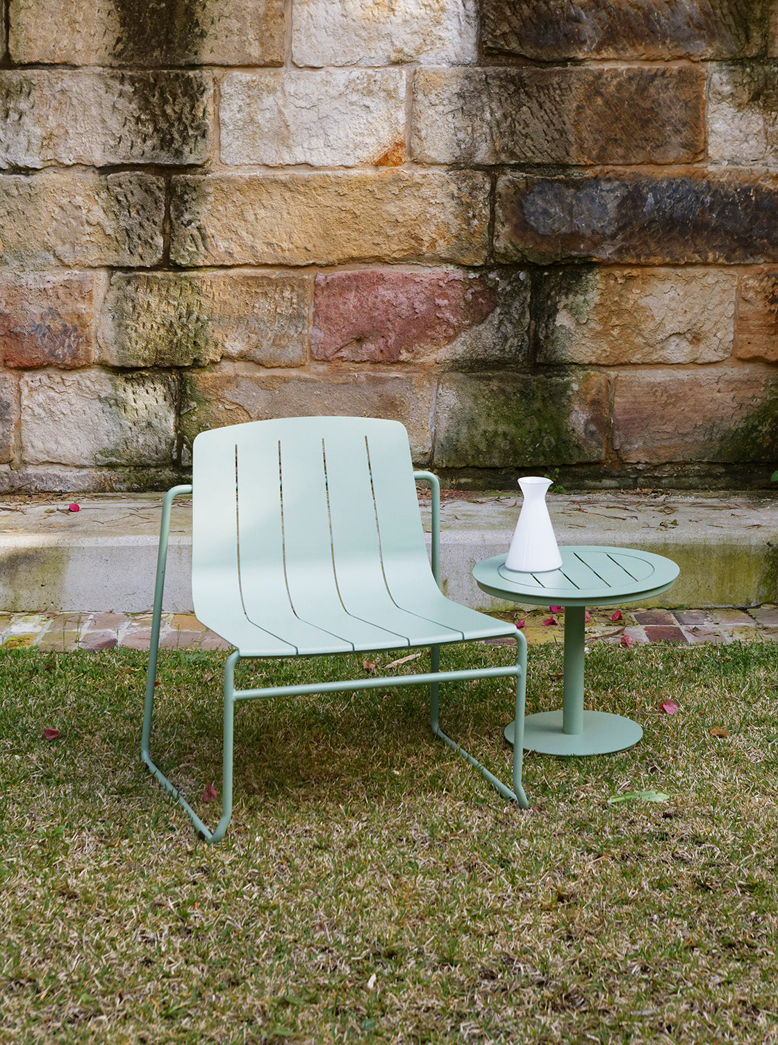 Light green outdoor chair and table set against a stone wall.