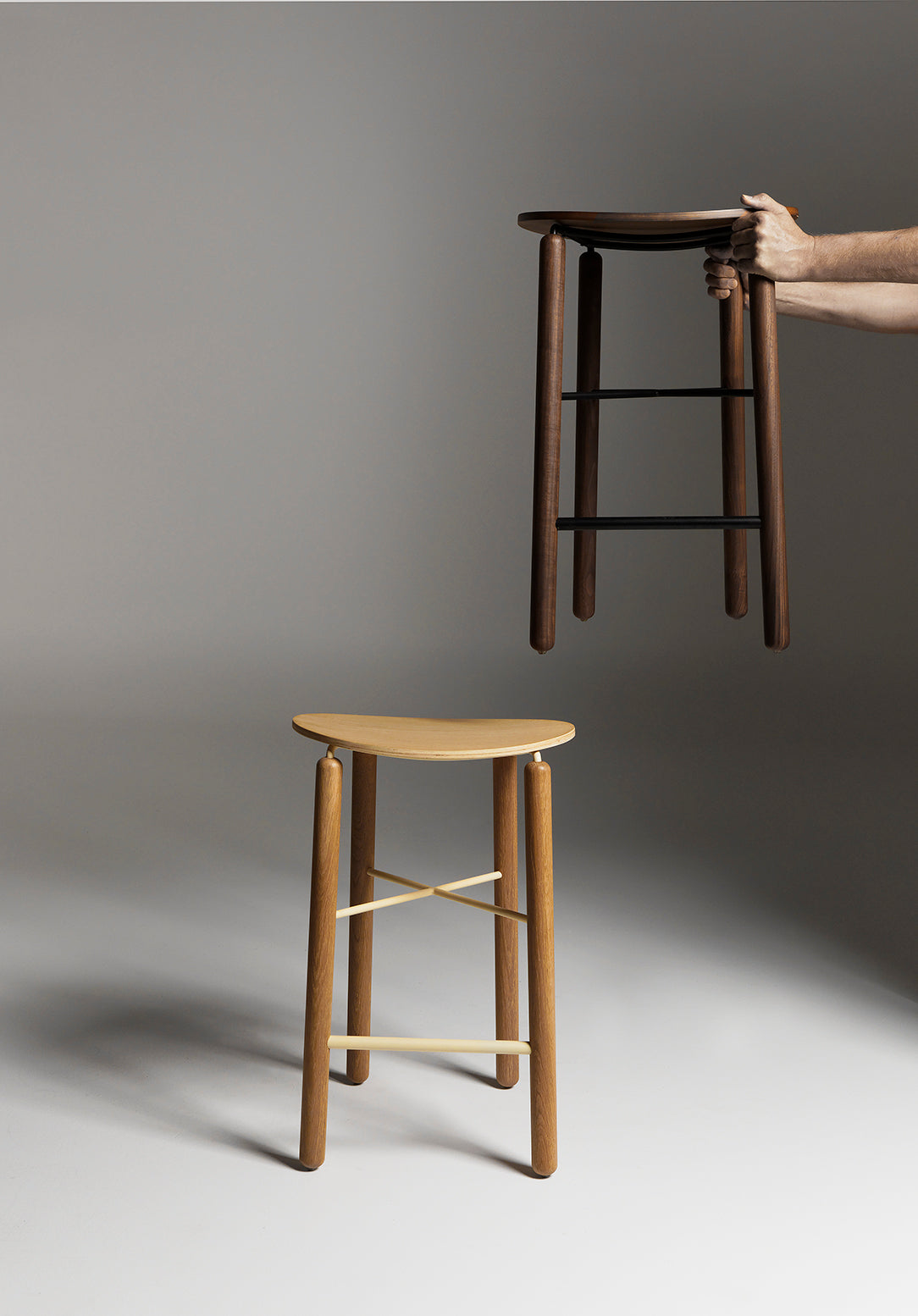 Person holding the Greta bar stool by the seat, showing its lightweight design and clean timber finish in oak and walnut options
