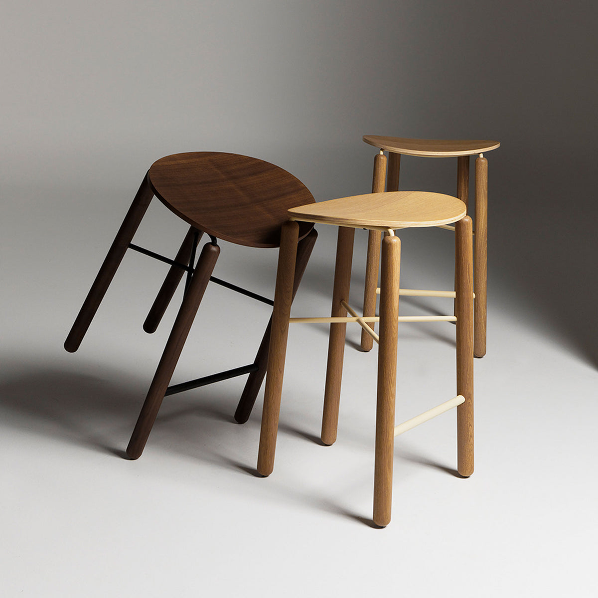 Angled studio shot of Greta stools in oak and walnut showing seat contours and slim metal frames