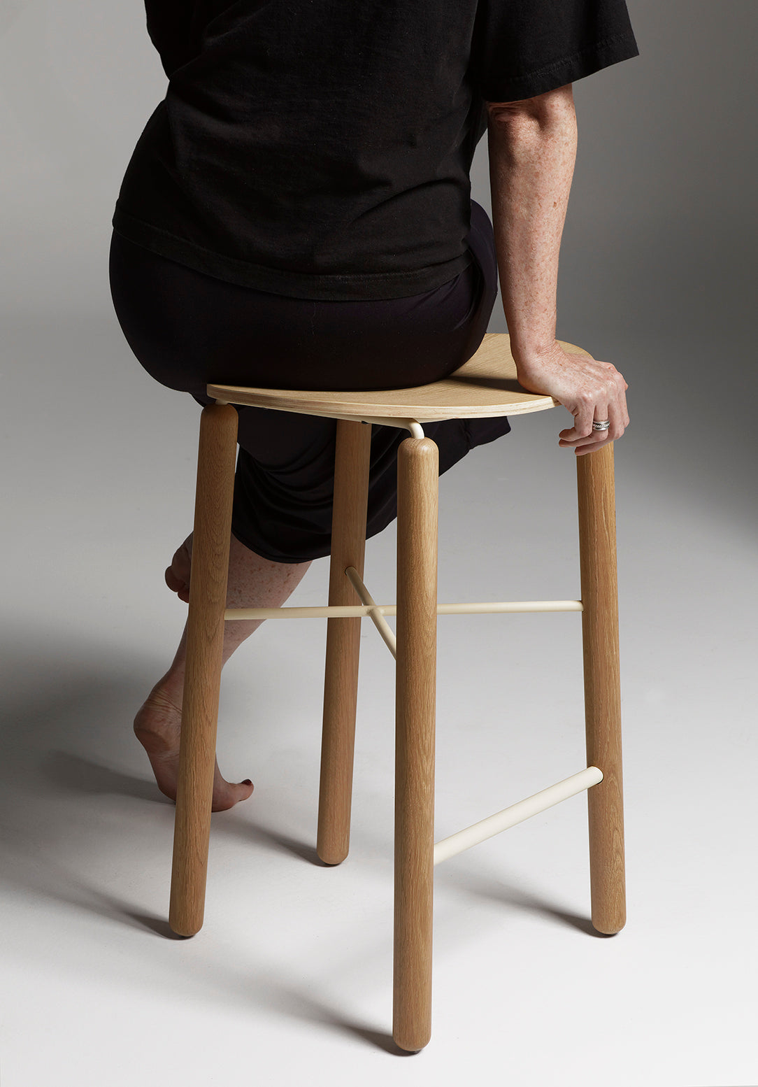 Person seated on the Greta bar stool in oak, showing comfort, seat height, and the natural timber finish in a casual setting