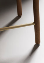 Close-up of the Greta bar stool in oak showing detailed view of the timber seat and slim black leg structure with footrest