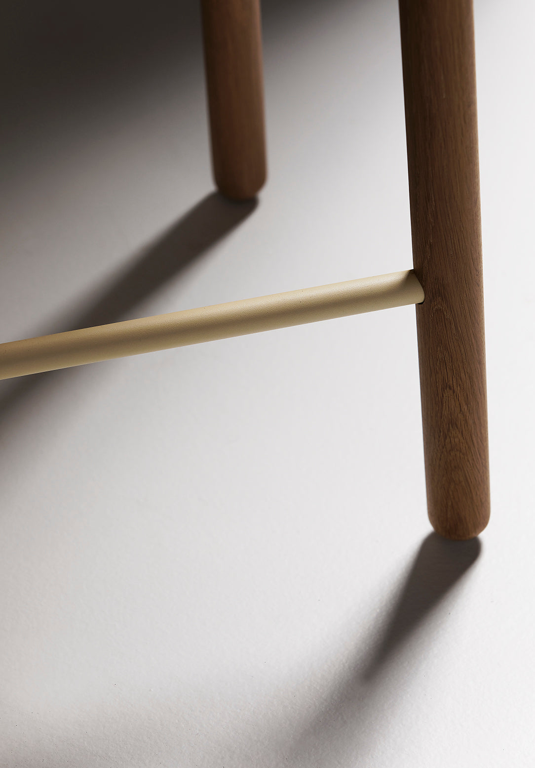 Close-up of the Greta bar stool in oak showing detailed view of the timber seat and slim black leg structure with footrest