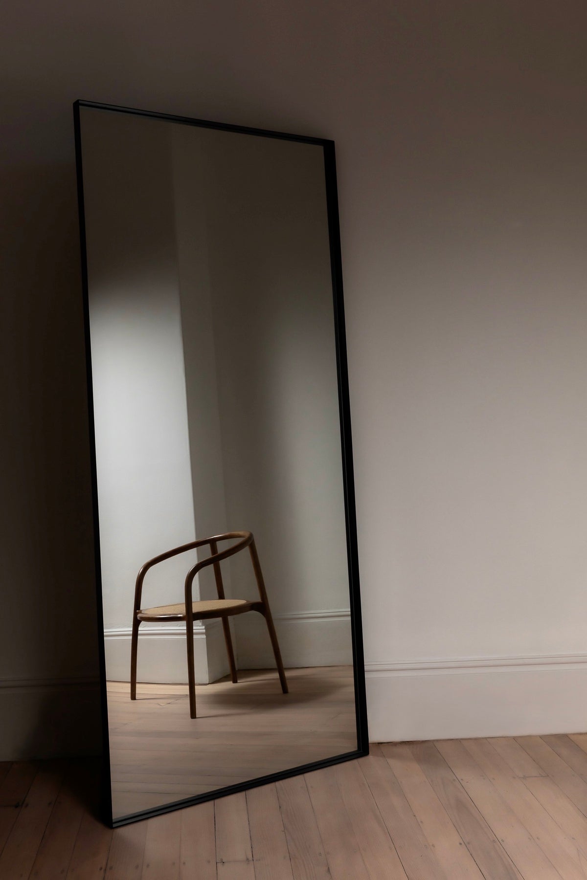 Luca Oversized Mirror in black leaning on timber floors, reflecting a timber chair