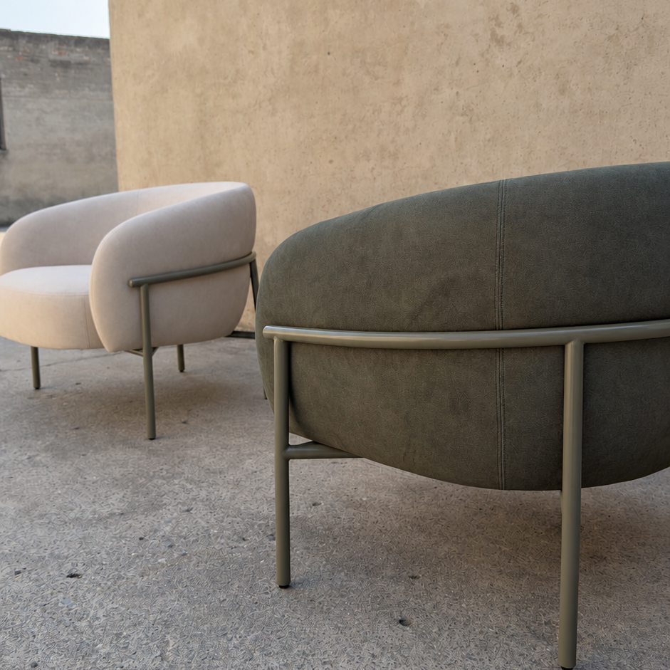 A modern outdoor lounge chair with a dark olive green upholstered seat and a light gray metal frame, shown next to another cream-colored chair against a stucco wall.