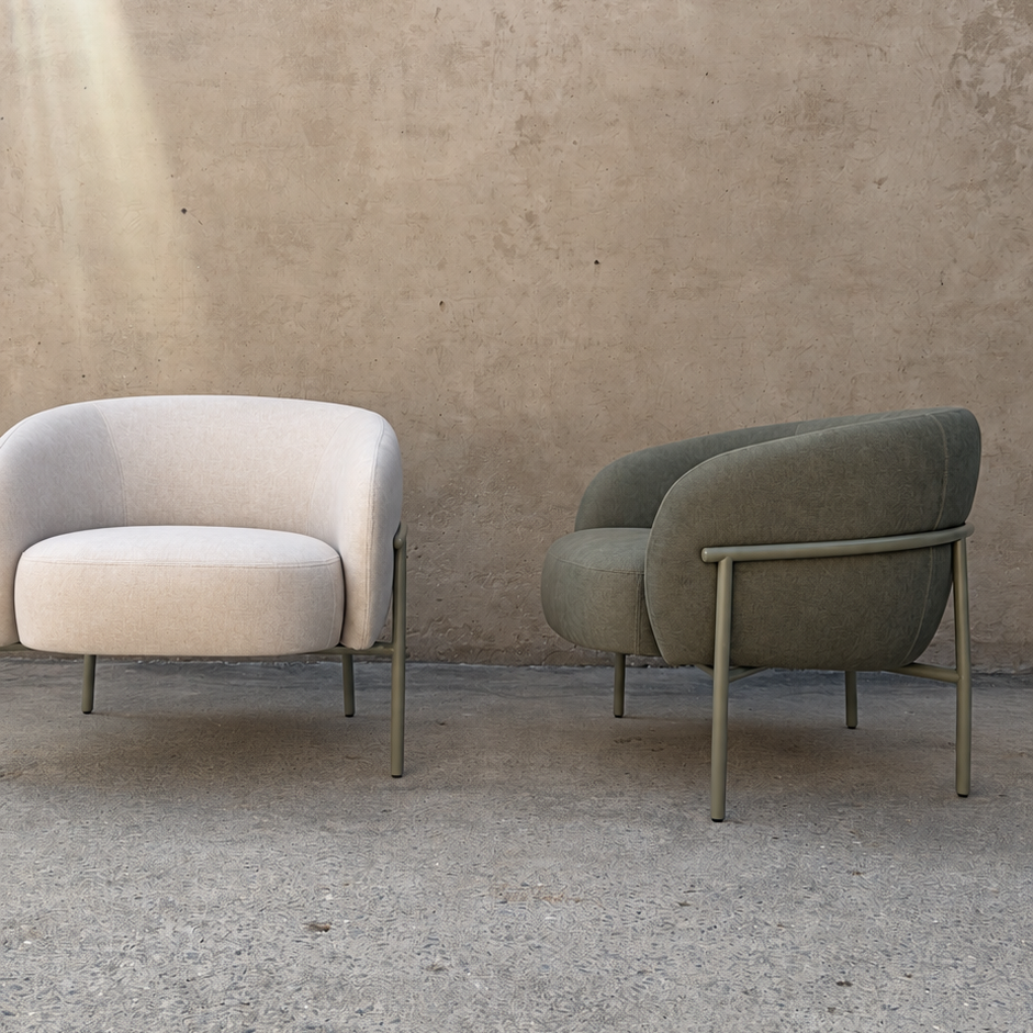 Two modern accent armchairs with curved backs and slim metal legs, set against a textured concrete wall and floor. The chair on the left is upholstered in a light cream fabric, and the chair on the right is upholstered in a muted sage green fabric.