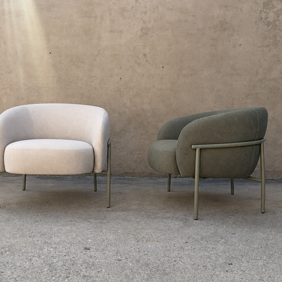 Two modern accent armchairs with curved backs and slim metal legs, set against a textured concrete wall and floor. The chair on the left is upholstered in a light cream fabric, and the chair on the right is upholstered in a muted sage green fabric.