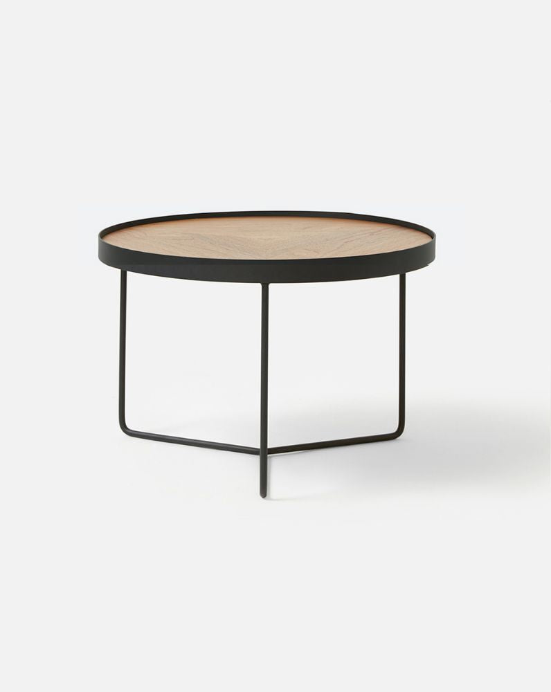 Close-up of the Greta stool in oak showing the curved timber seat and slim black metal leg with footrest, highlighting material detail and construction