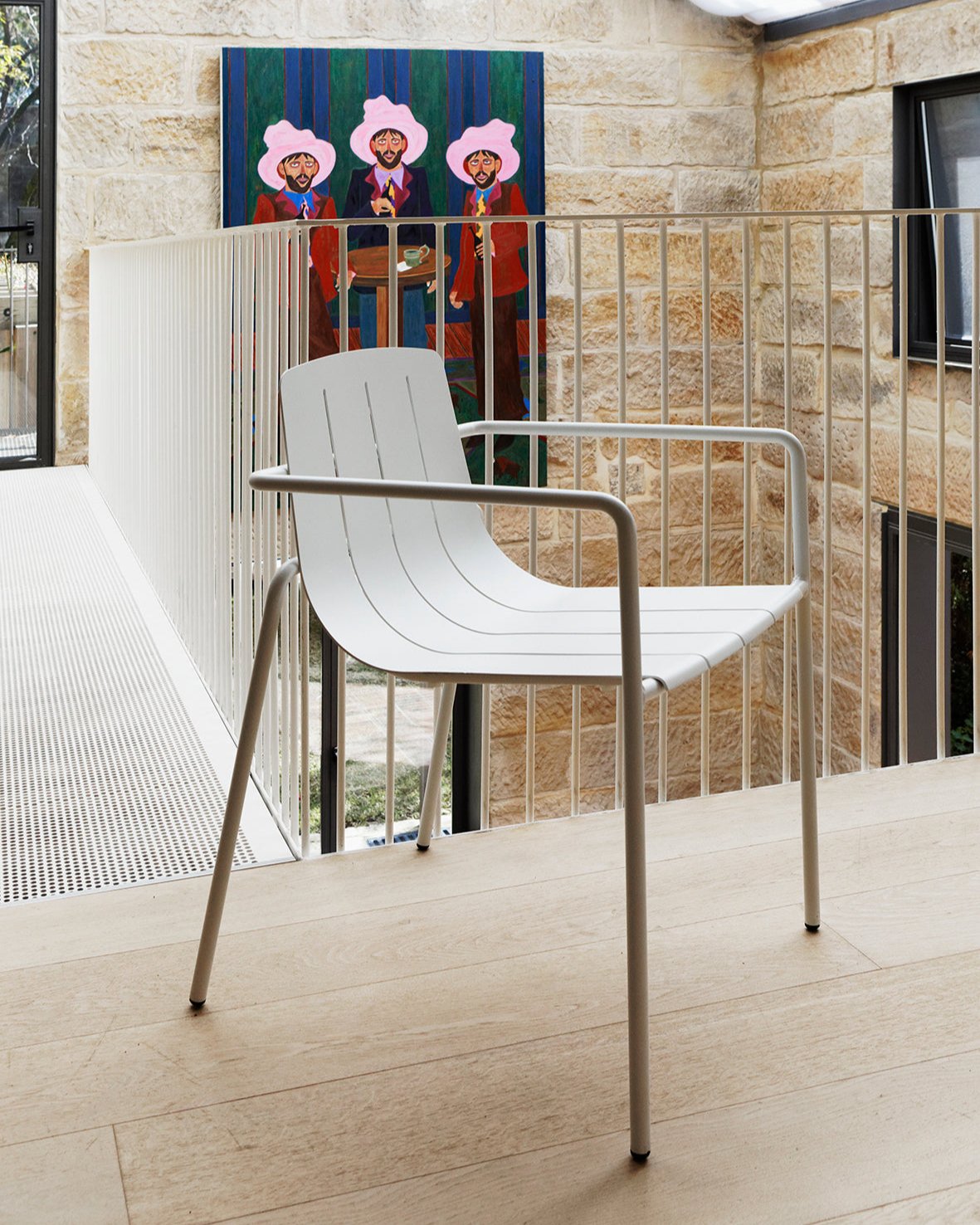 A modern white Remy Armchair with slim integrated armrests, made of metal, placed in a room with a decorative wall painting in the background.