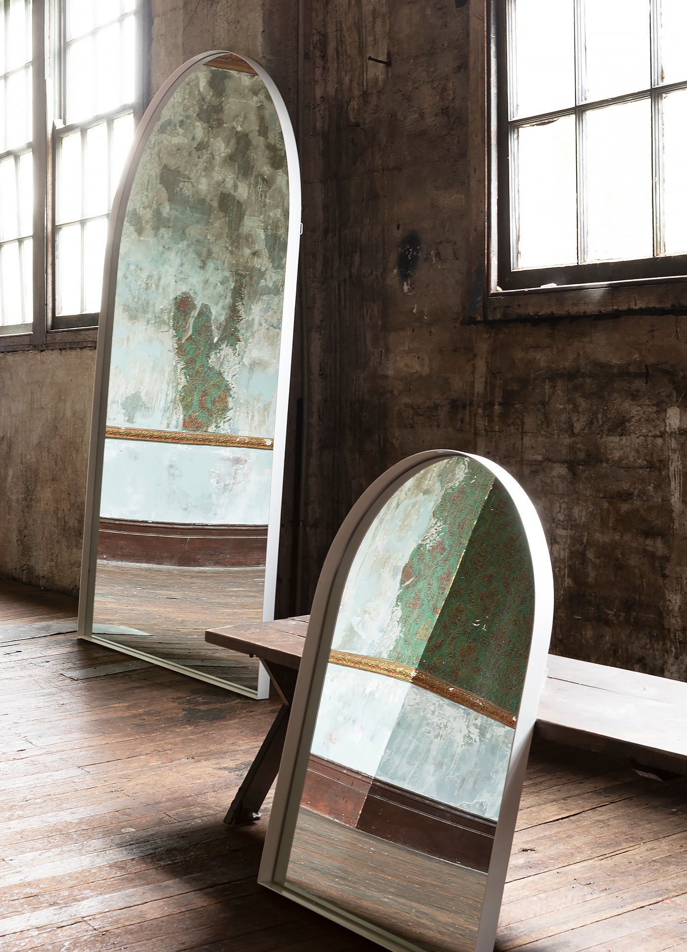 White full length arch mirror standing against white wall in industrial studio space