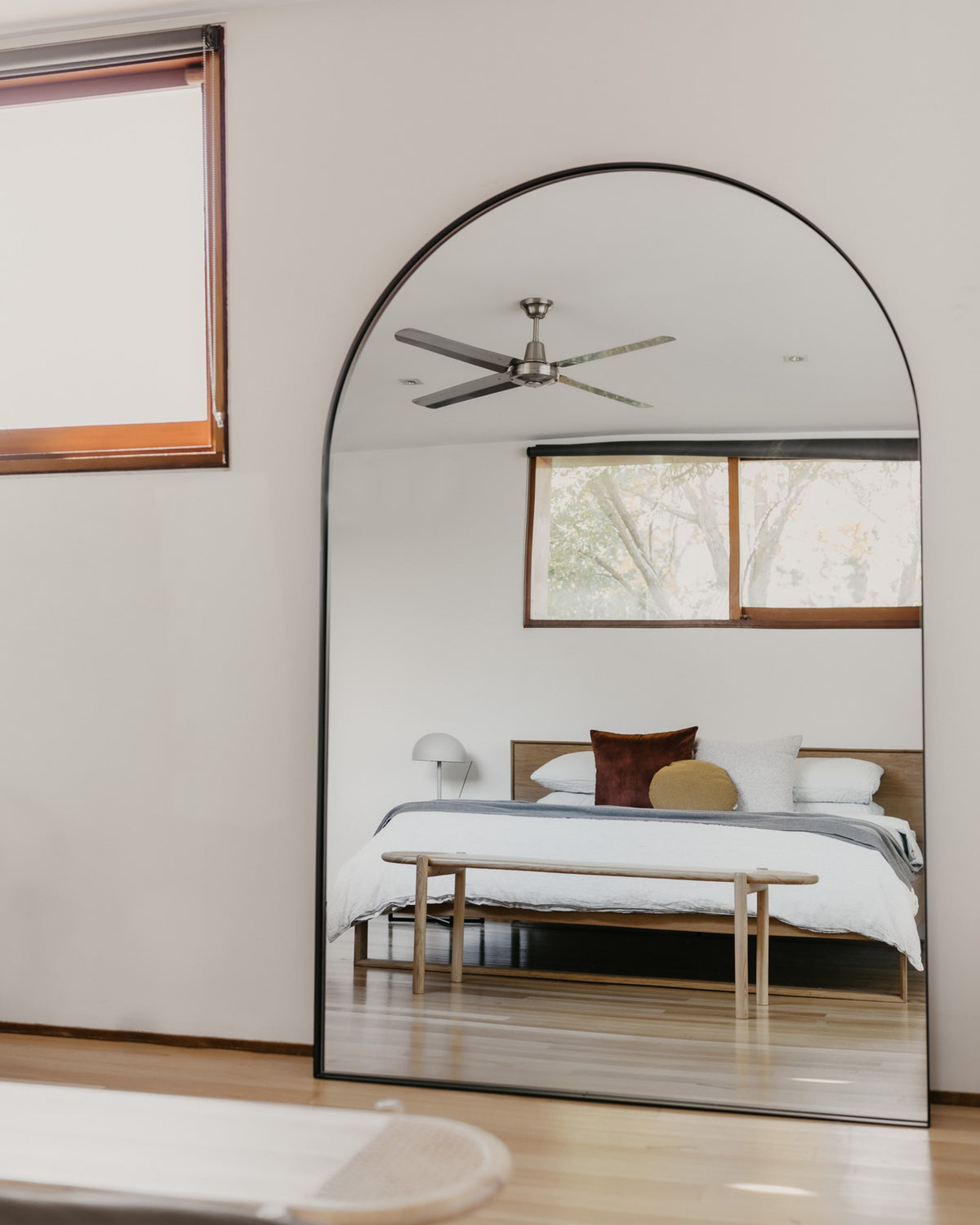 Archie Oversized Mirror in black leaning in a bedroom, reflecting a bed and window