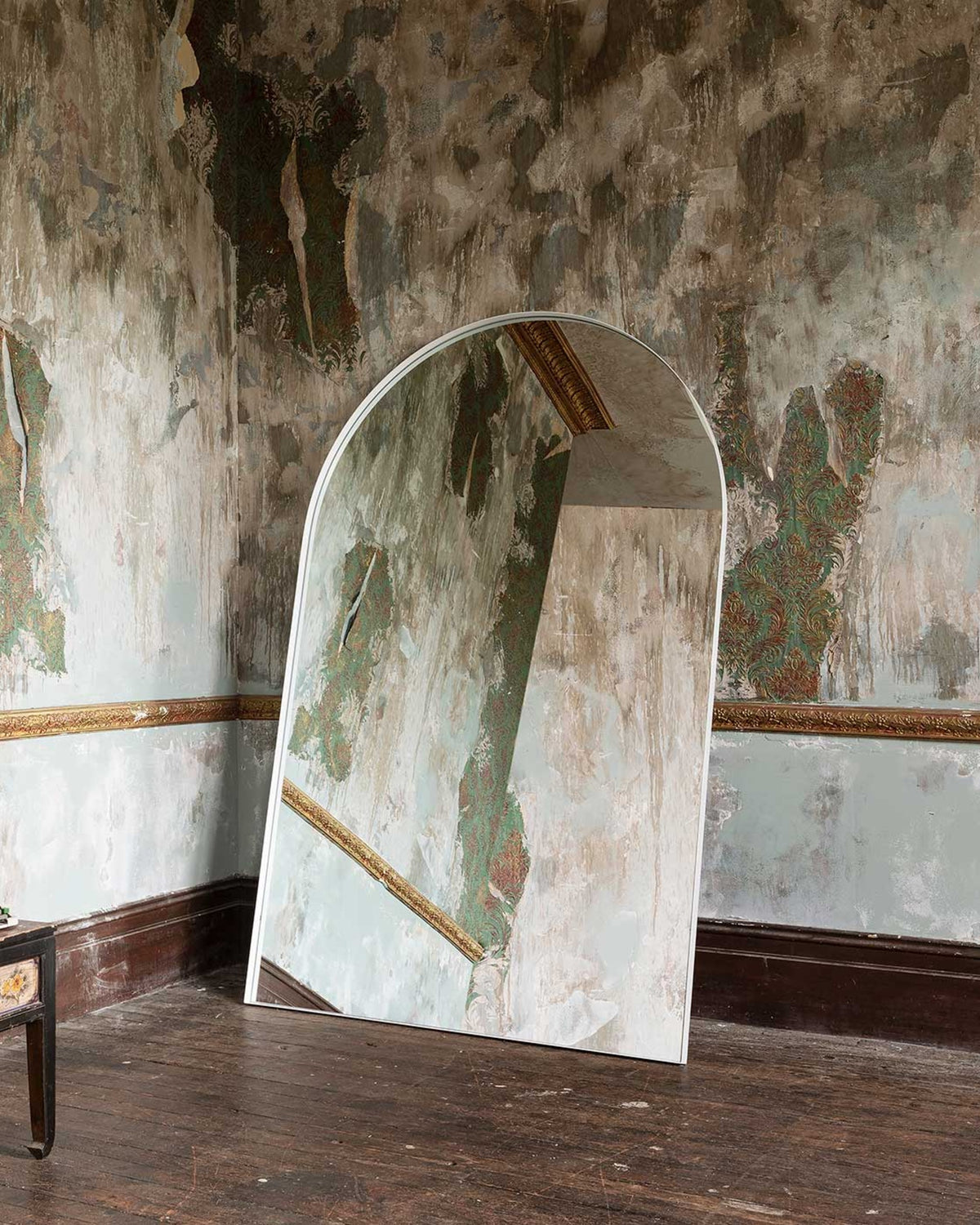 Archie Oversized Mirror in white leaning in a heritage room with peeling wallpaper