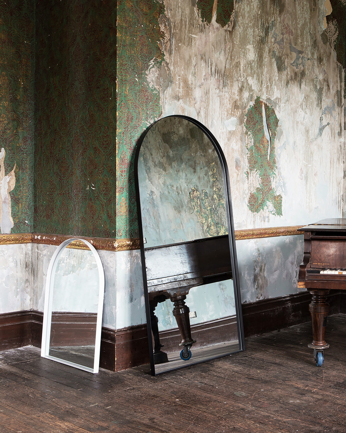 Archie Standard Mirror in black beside the white Archie mirror in a room with a grand piano