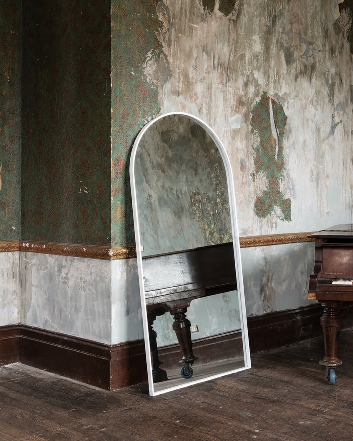 Archie Standard Mirror in white leaning in a heritage room, reflecting a grand piano